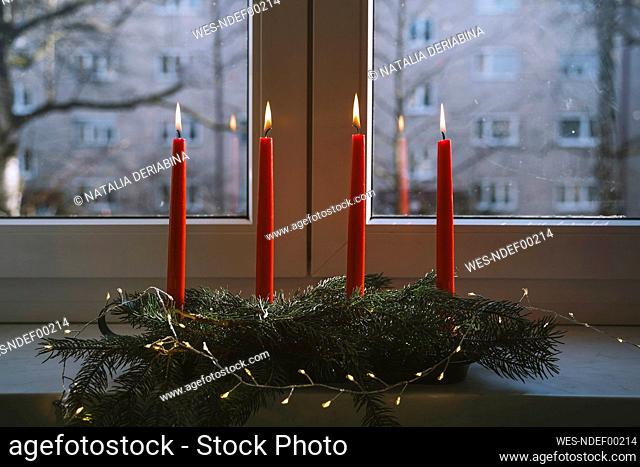 Burning red candles on advent wreath in front of window at home