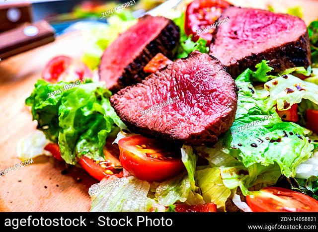 Served steak salad with beef meat and fresh organic lettuce leaves and cherry tomatoes on concrete background with copy space