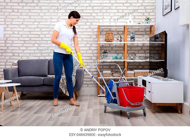 Female Janitor Cleaning Floor With Mop In Living Room