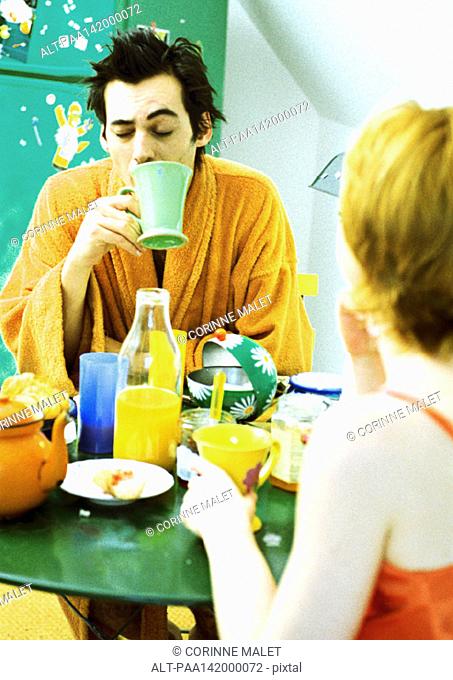 Young couple sitting at table having breakfast, woman in rear view