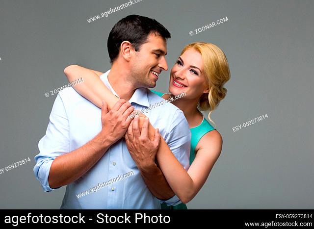 Beautiful young couple hugging. Blond woman in mint dress and handsome man in shirt and trousers standing on grey background. Valentine's day concept