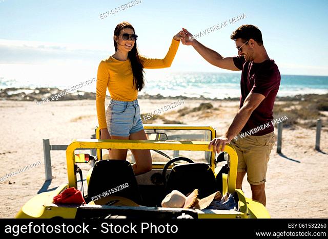 Happy caucasian couple in beach buggy by the sea holding hands