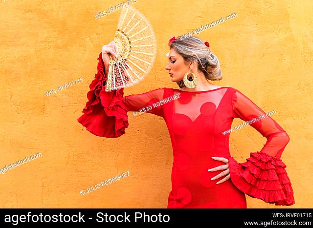 Female dancer with hand fan standing in front of wall