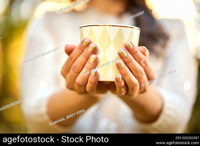 woman in a white sweater holds in her hands a mug of hot tea in an autumn forest