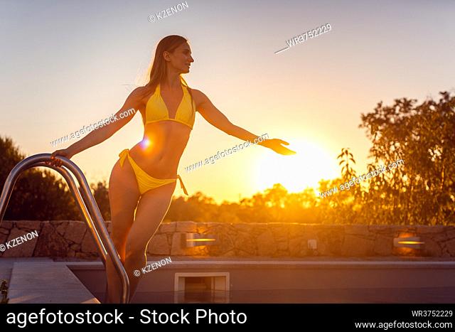 Beautiful woman getting into a swimming pool during sunset making for a romantic scene