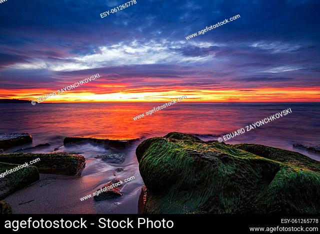Sea sunrise with rocks with moss on the beach