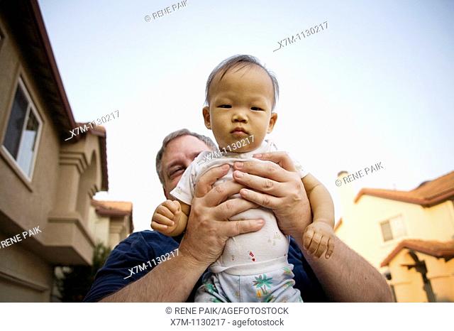A tiny Korean baby boy being held in a Caucasian man's giant hands