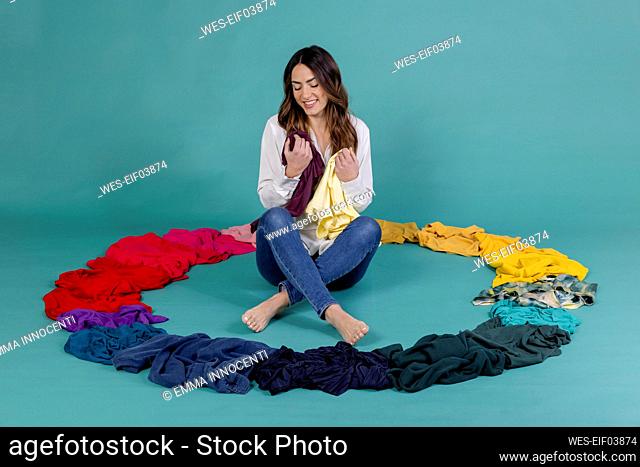 Happy woman with t-shirt sitting inside circle made of clothes against blue background