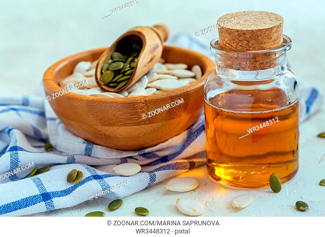 Organic pumpkin seed oil in a bottle and pumpkin seeds in a wooden bowl on linen cloth, selective focus