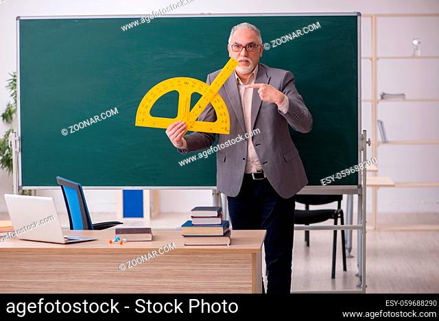 Old teacher holding line in front of blackboard