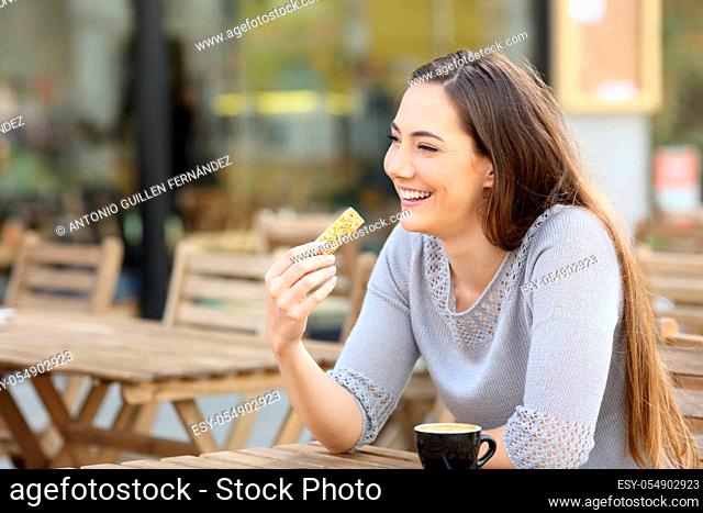 Happy young woman holding a cereal snack bar sitting on a cafe terrace