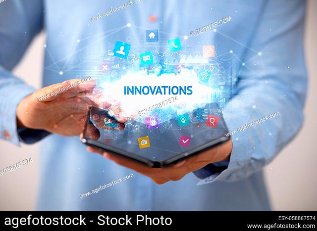 Businessman holding a foldable smartphone with INNOVATIONS inscription, technology concept
