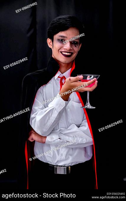 Portrait of asian young adult teenage man wear Halloween costume cloth hold glass of cocktail for Halloween party background