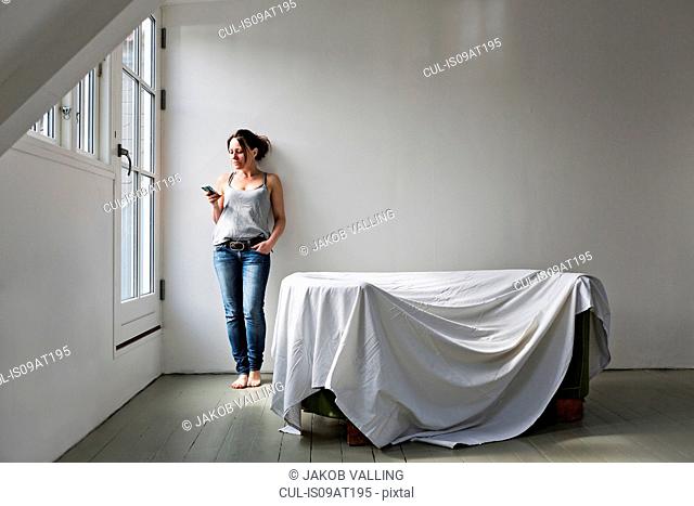 Mature woman standing in part furnished home, using mobile phone