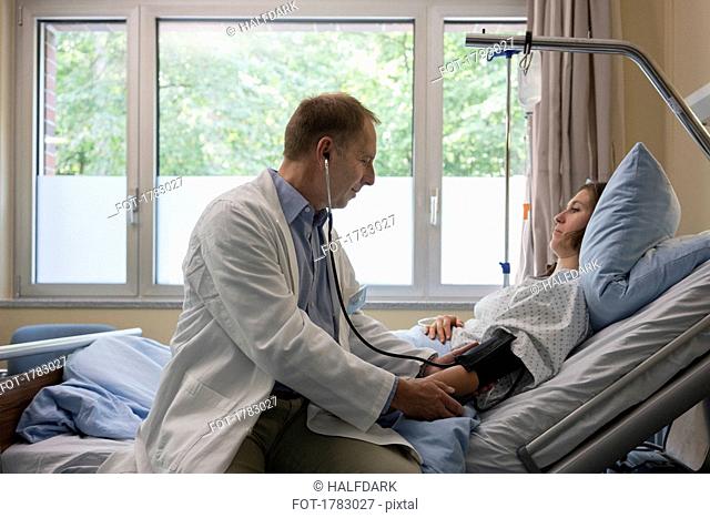Doctor making rounds, checking blood pressure of patient in hospital room