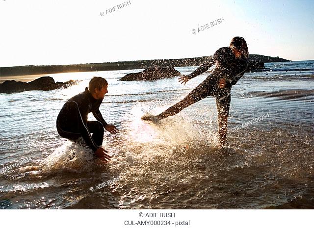 Couple in wetsuits splashing in shallow water