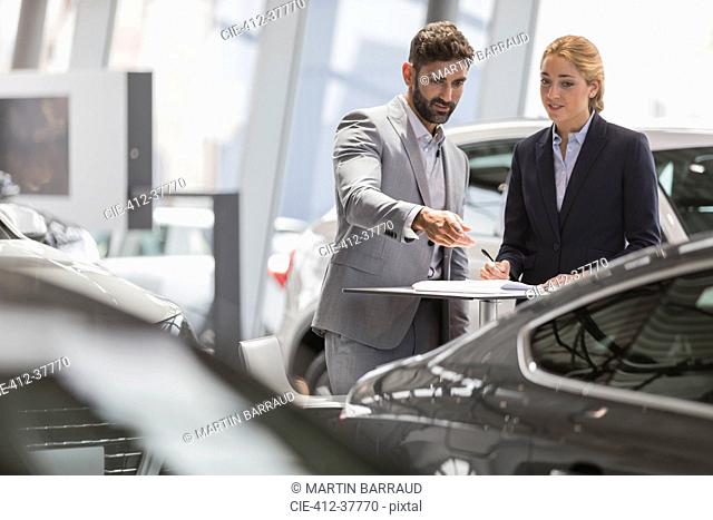 Car sales people meeting, examining new car in car dealership showroom