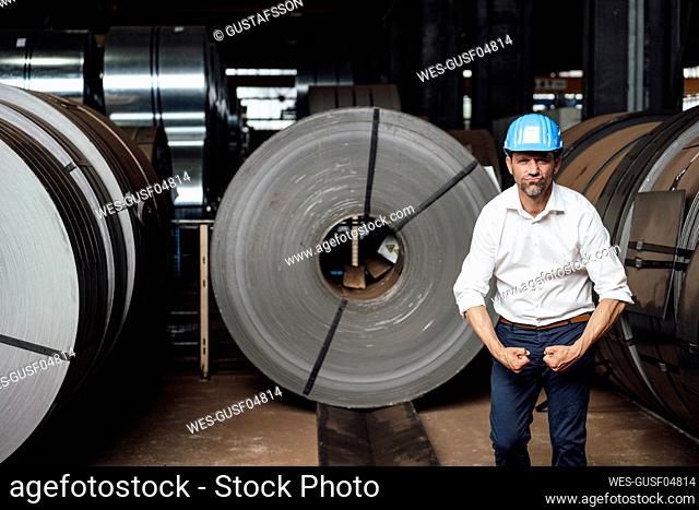 Businessman flexing muscles while standing in factory