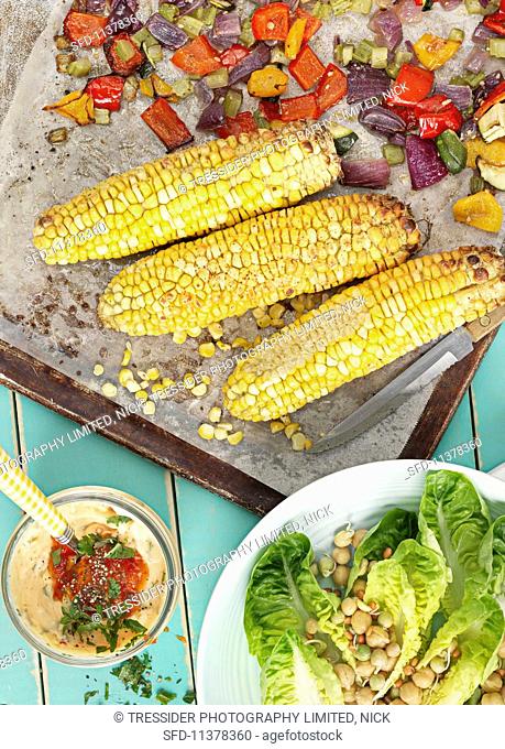 Oven-roasted vegetables and corn cobs with a salad and a dip