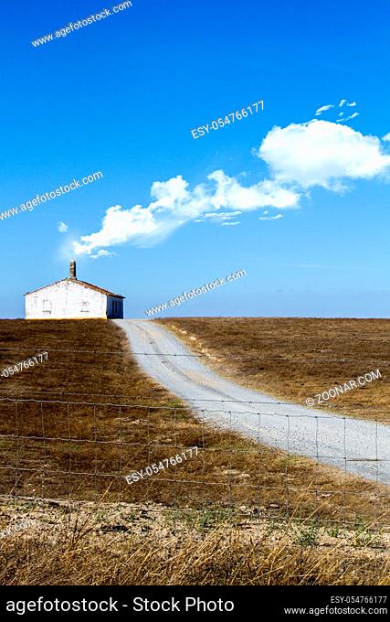 View of a conceptual photo with a lonely house with road on a dry land with white clouds exiting the chimney