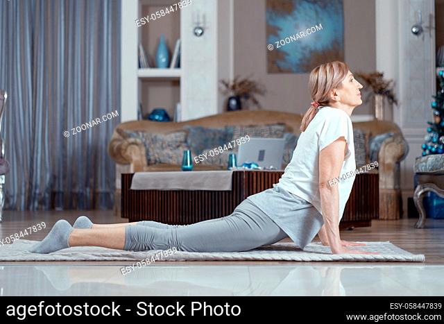 Yoga Classes For Women Over 50 Years. A Woman is Engaged at Home in the Living Room. On the Carpet She Took the Position of Asana