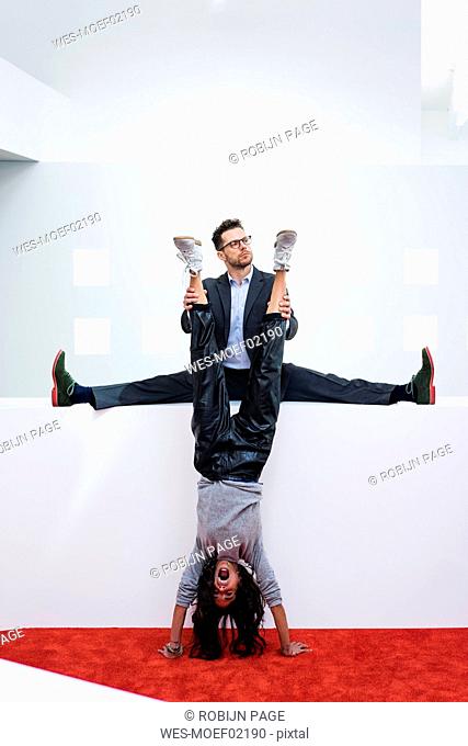 Businessman in office holding woman's legs doing a handstand