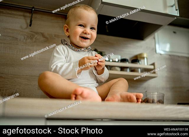 Happy cute baby girl sitting on kitchen counter at home