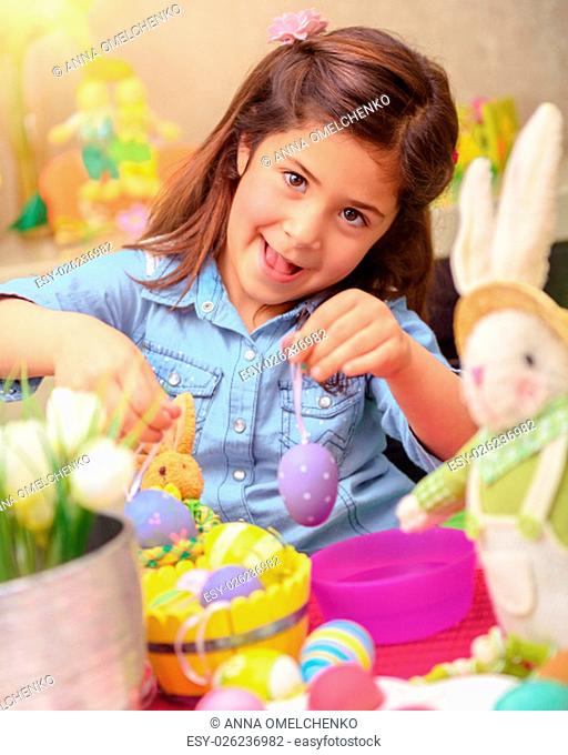 Portrait of cute little girl decorating Easter eggs by different colors, having fun at home with bunny toy, drawing lesson in daycare
