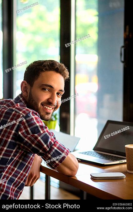 Portrait of happy handsome man working on laptop computer in restaurant or cafe. Cheerful man smiling for camera