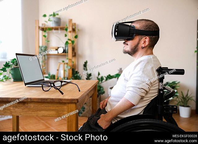 Man with disability wearing virtual reality simulator in front of laptop at home