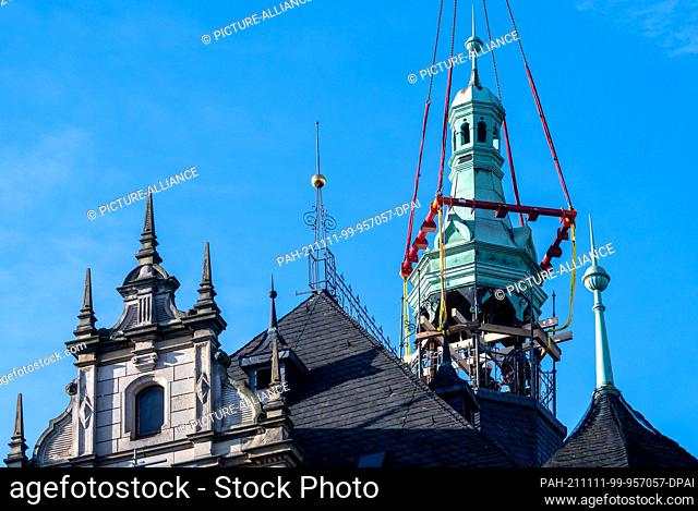 11 November 2021, Saxony-Anhalt, Halle (Saale): The spire of the town house in Halle/Saale hovers on the crane hook from the building onto the market