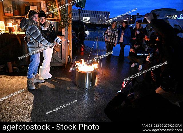 12 December 2023, Bavaria, Munich: Cathy Hummels (2nd from left) and her sister Vanessa (left) warm their hands at a fire during their charity Christmas...