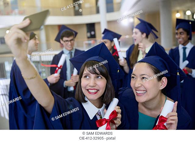 College women graduates in cap and gown taking selfie with diplomas