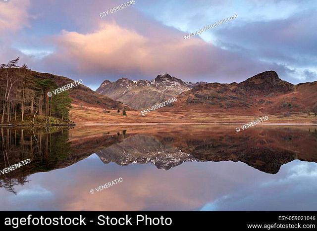 Beautiful Winter sunrise over Blea Tarn in Lake District with snow capped Langdale Pikes in distance