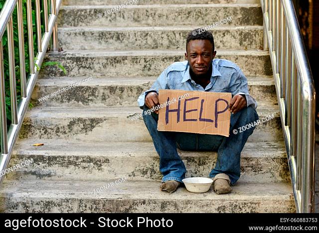 Portrait of young homeless African man on stairs in the streets outdoors