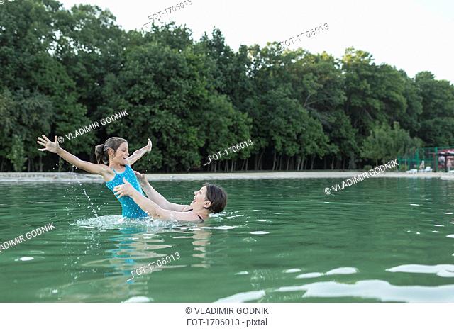 Grandmother enjoying with granddaughter in swimming pool against trees