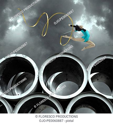 Woman gymnast outdoors on large cement cylinders jumping with ribbon