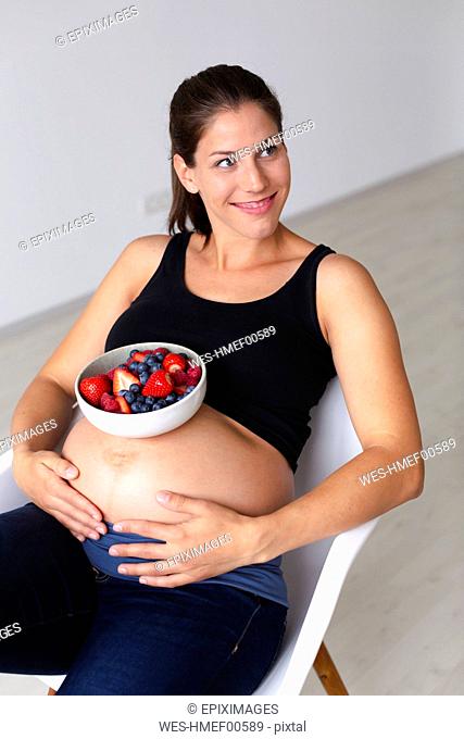 Young pregnant woman is eating different kinds of fresh fruits