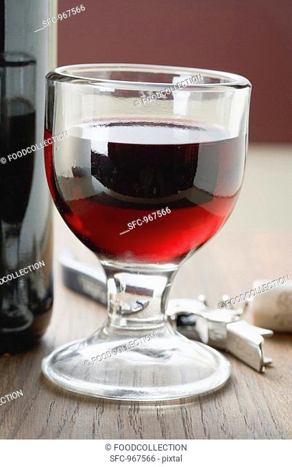 Glass of red wine between bottle and corkscrew