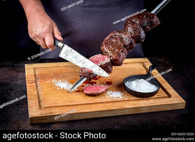 Traditional barbecue dry aged wagyu Brazilian picanha from the sirloin cap of rump beef sliced by a chef directly from the skewer as close-up on a wooden...