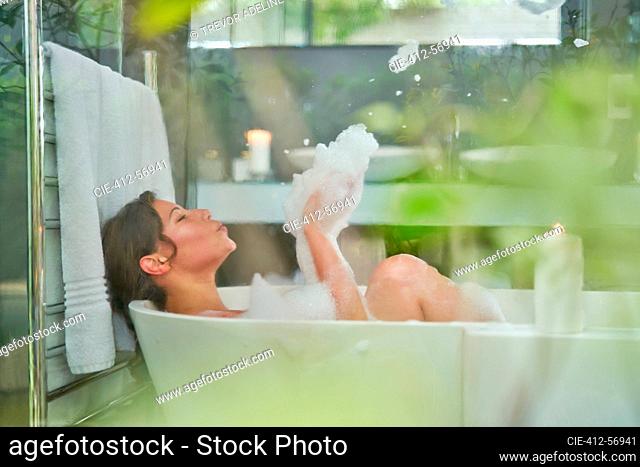 Playful woman in bubble bath in luxury soaking tub in bathroom
