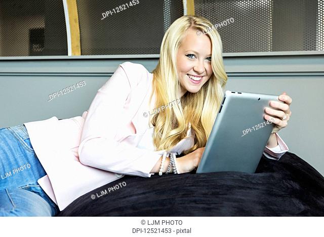 Business portrait of a beautiful young millennial businesswoman with long blond hair holding a tablet and posing for the camera in the workplace; Sherwood Park