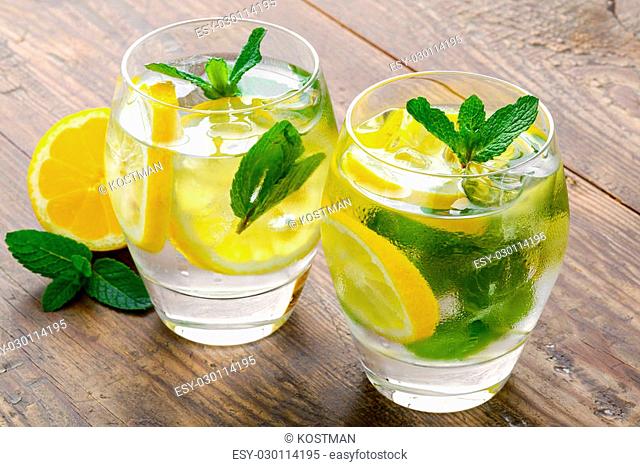 Preparation of the lemonade drink. Lemonade in two glass and lemon with mint on the table outdoor
