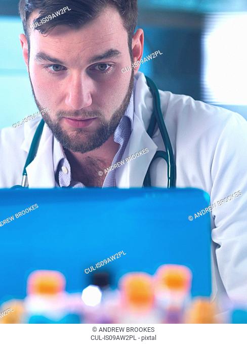 Doctor reading patient medical test results on laptop, samples in foreground
