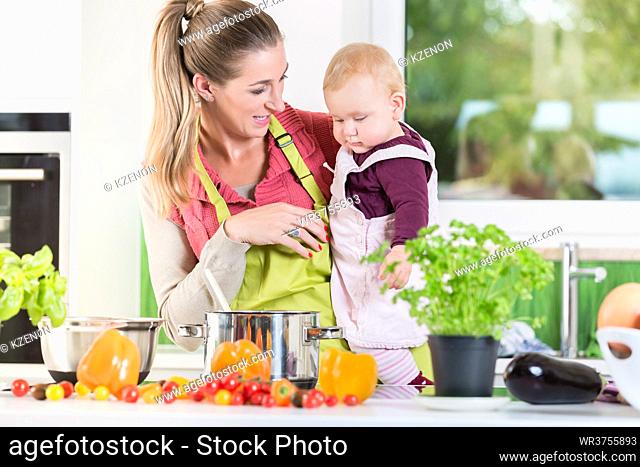Happy mother working in kitchen while carrying child