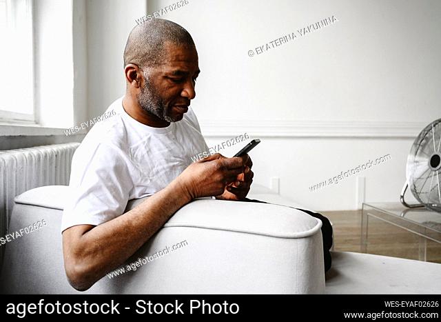Mature man using smart phone on sofa at home
