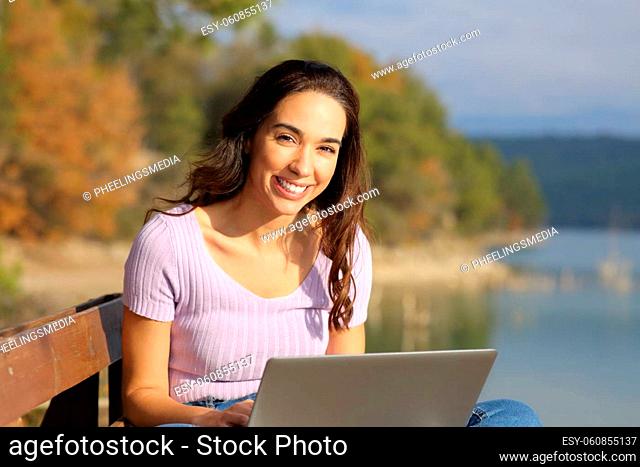 Happy woman with a laptop looks at you sitting outdoors in the mountain