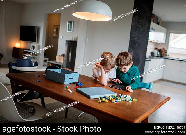 Boys sitting together at table and using digital tablet