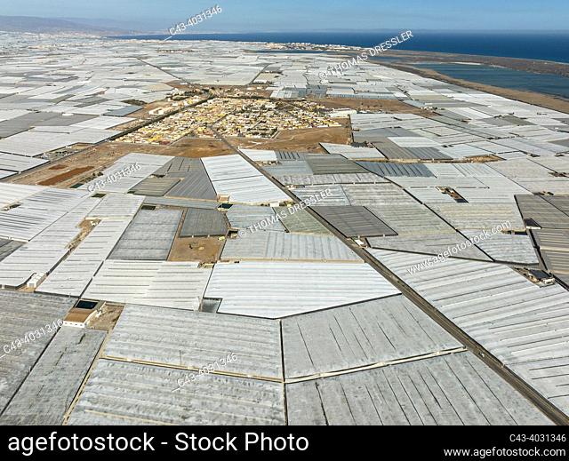 The town of San Agustin amidst masses of shimmering plastic greenhouses. On the right the shallow lagoon Salinas de Cerrillos. Aerial view. Drone shot
