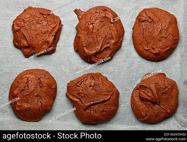 Close up several freshly baked round brownie chocolate cookies on baking paper, elevated top view, directly above